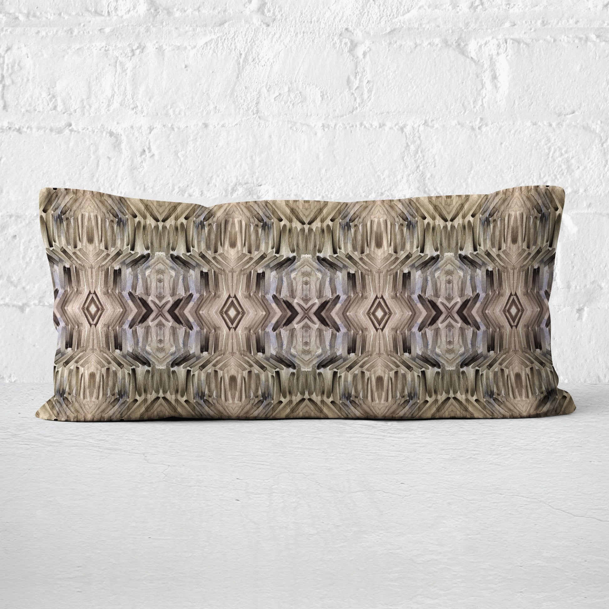 12x24 rectangular pillow featuring a brown abstract hand-painted pattern leaning up against a white brick wall.