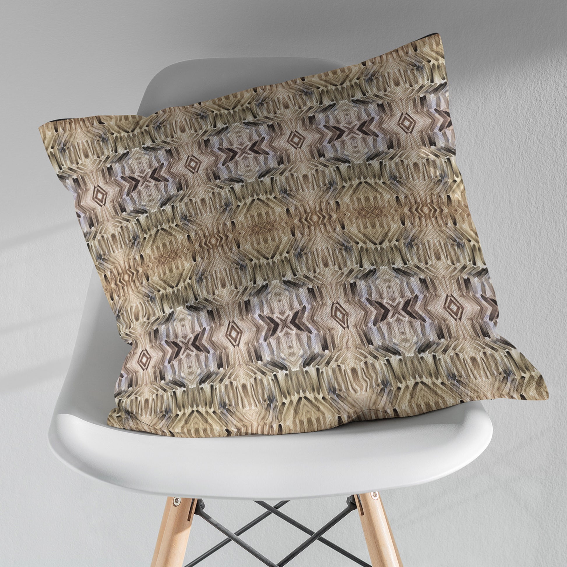 Pillow featuring abstract hand-painted pattern in neutral tones, sitting on a white modernist chair