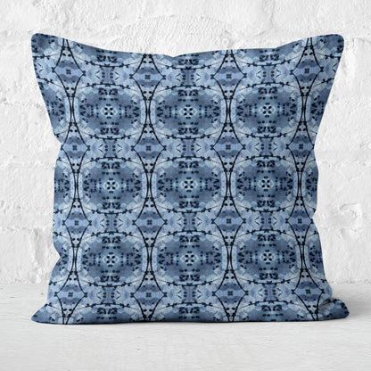 Square throw pillow featuring a blue and black abstract pattern sitting in front of a white brick wall