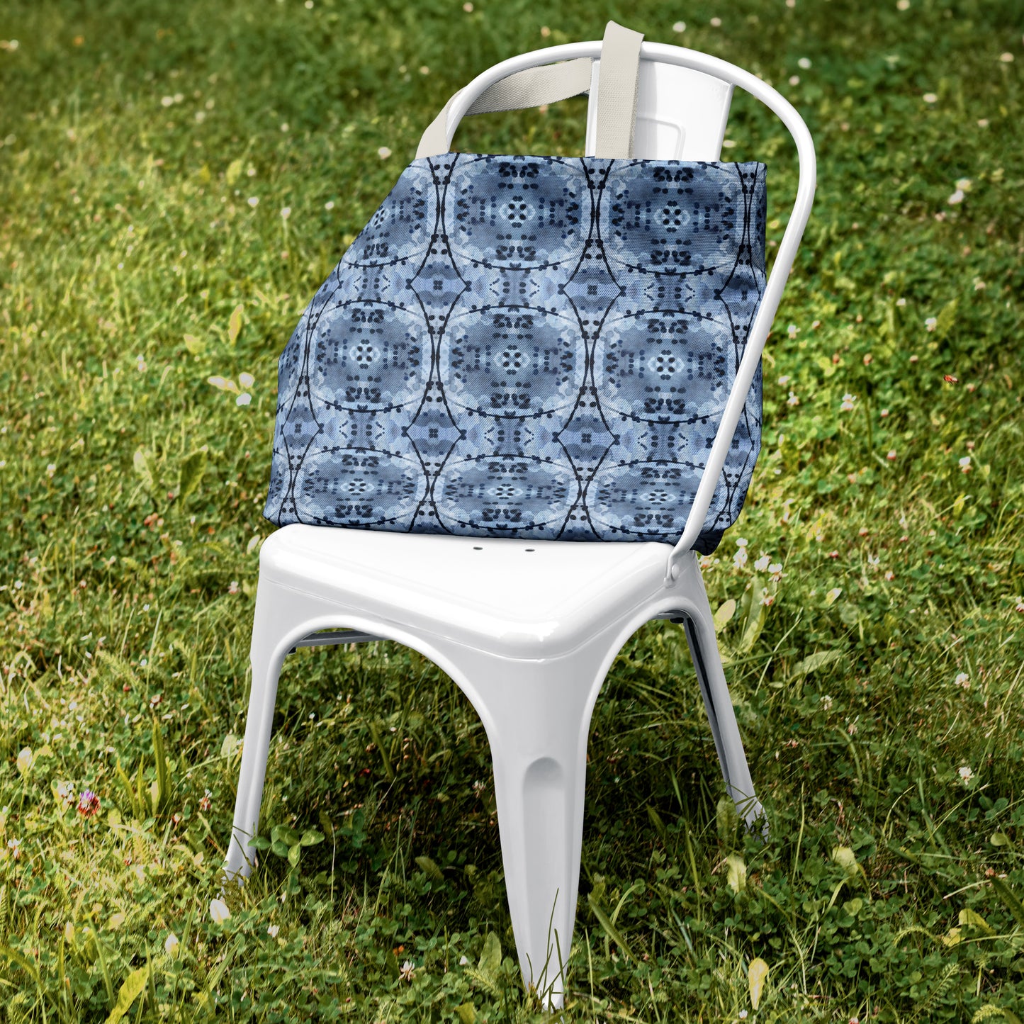 Large tote bag featuring an abstract hand-painted blue design, sitting on a white chair against a green grass background