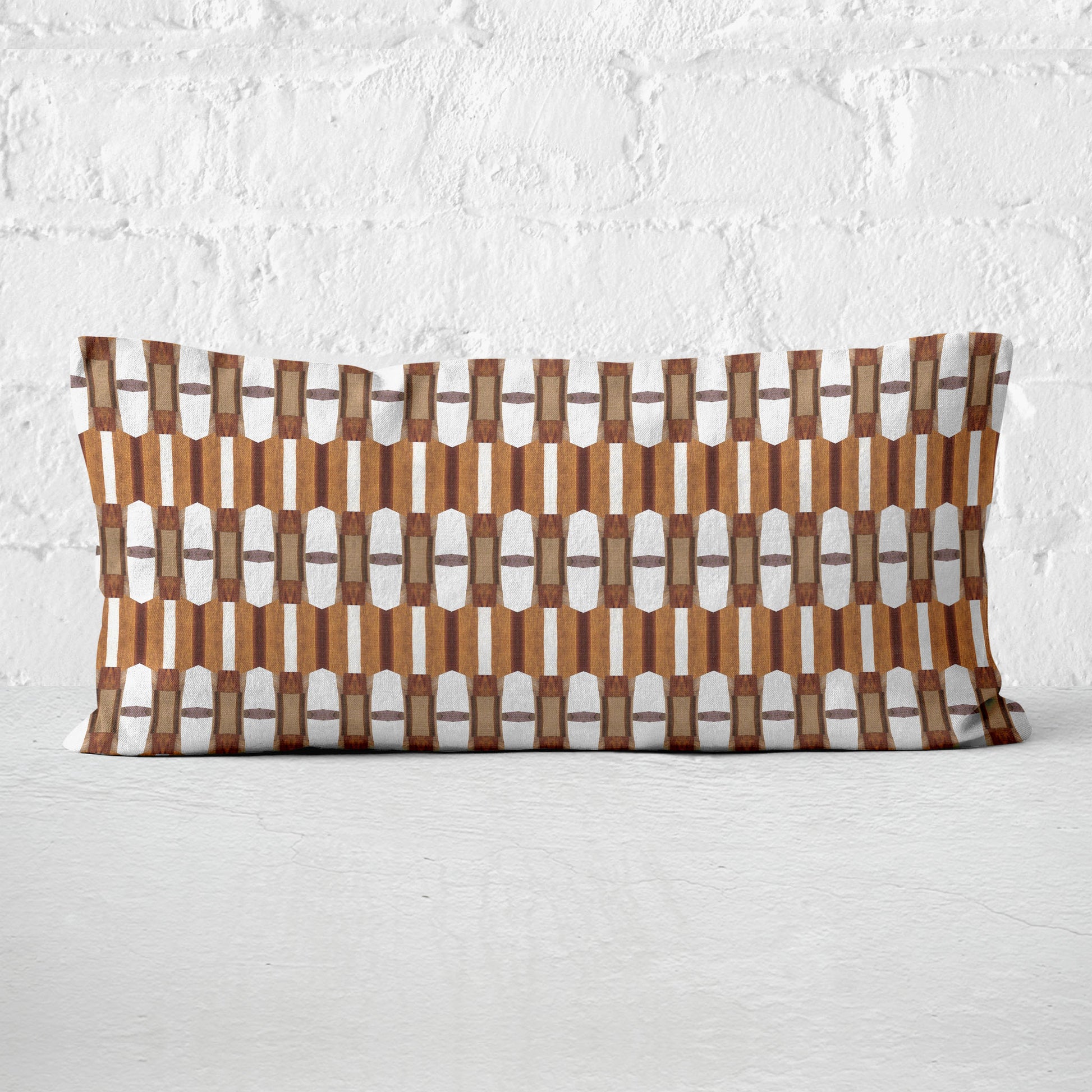 12x24 Lumbar pillow featuring a brown and white collaged pattern leaning against a white brick wall