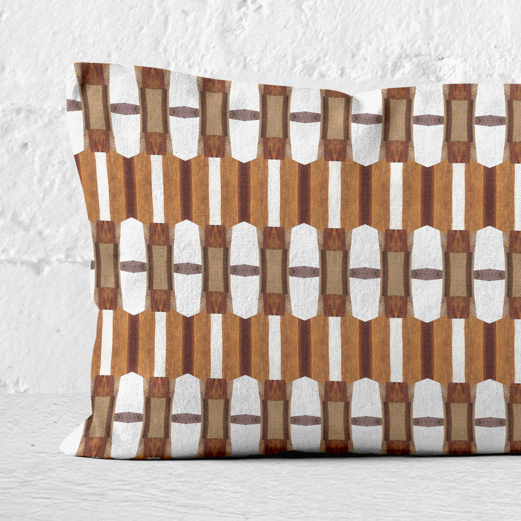 Detail of a 12x24 lumbar pillow featuring a brown and white collaged pattern leaning against a white brick wall.