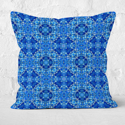 Square throw pillow featuring a hand-painted pattern mosaic pattern in cobalt blue and white brick wall in the background