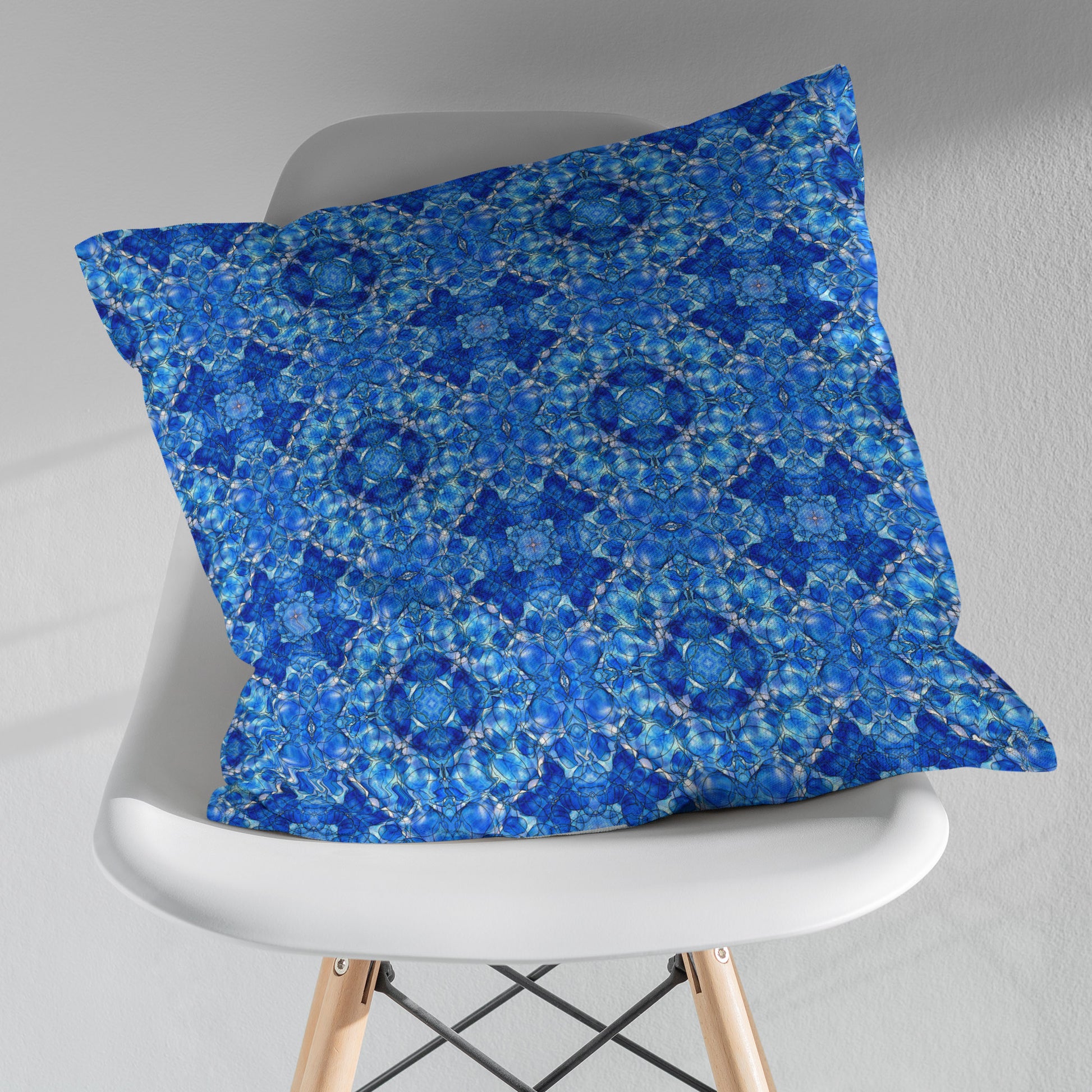 Square throw pillow featuring a hand-painted pattern mosaic pattern in cobalt blue, sitting on a white modernist chair