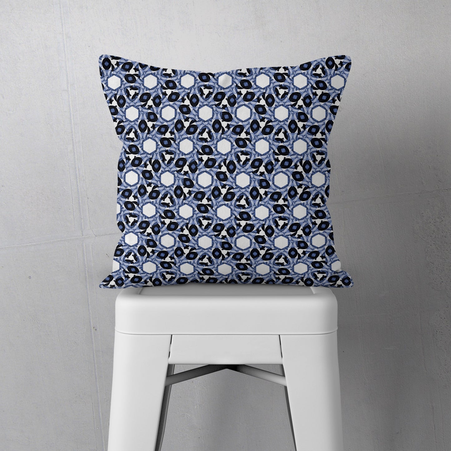 Throw pillow featuring abstract geometric blue and white pattern, sitting on a white metal stool