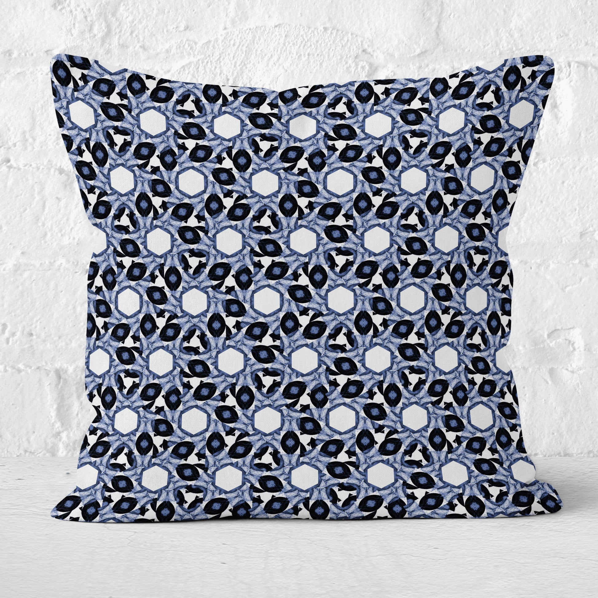 Throw pillow featuring abstract geometric blue and white pattern with a white brick wall in the background