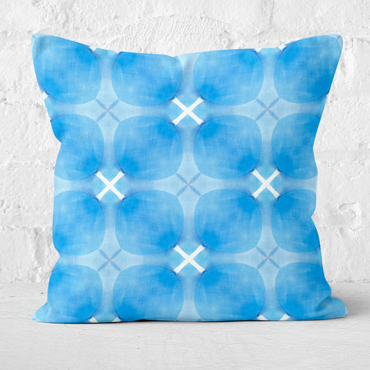 Square throw pillow with blue circular pattern on white brick background