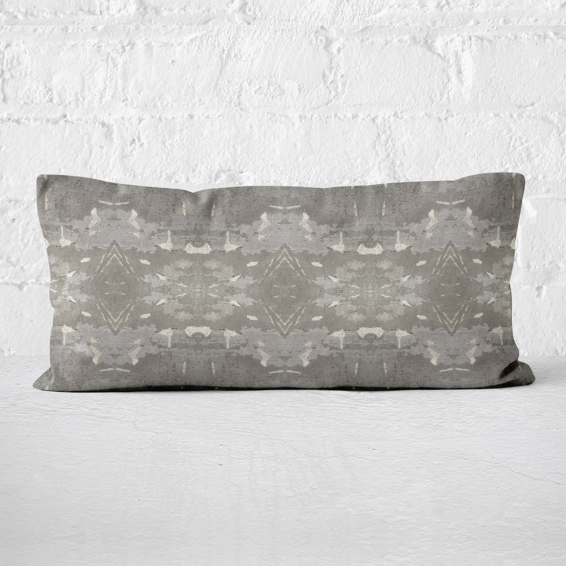 Lumbar pillow featuring a grey abstract geometric pattern leaning against a white brick wall