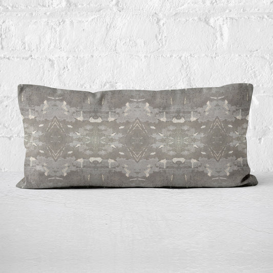 Lumbar pillow featuring a grey abstract geometric pattern leaning against a white brick wall