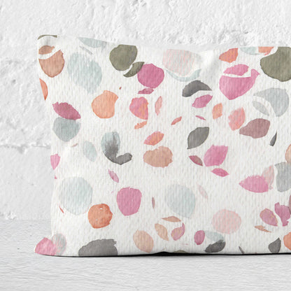 Close up detail of a 12x24 lumbar pillow, featuring an abstract watercolor painting of flower petals, leaning against a white brick wall.