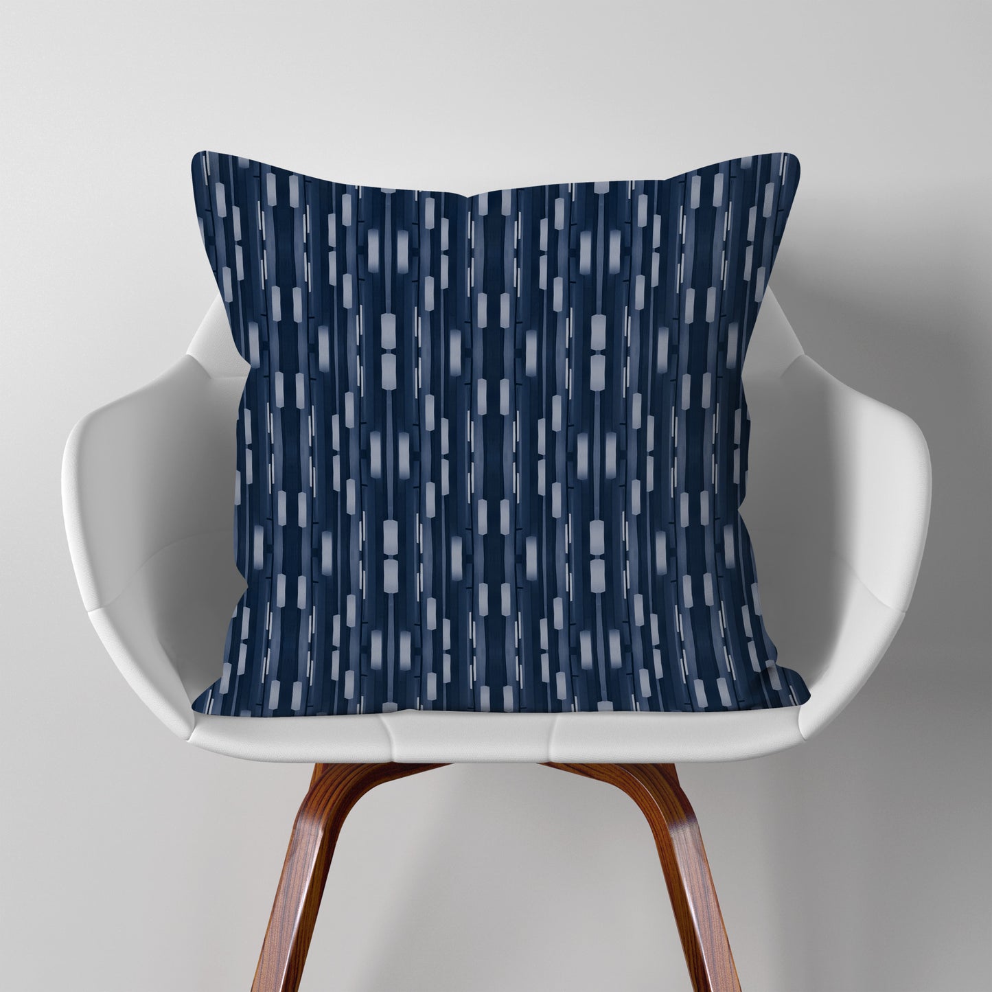 Pillow featuring collaged stripe pattern in blue and white, sitting on a modern white chair