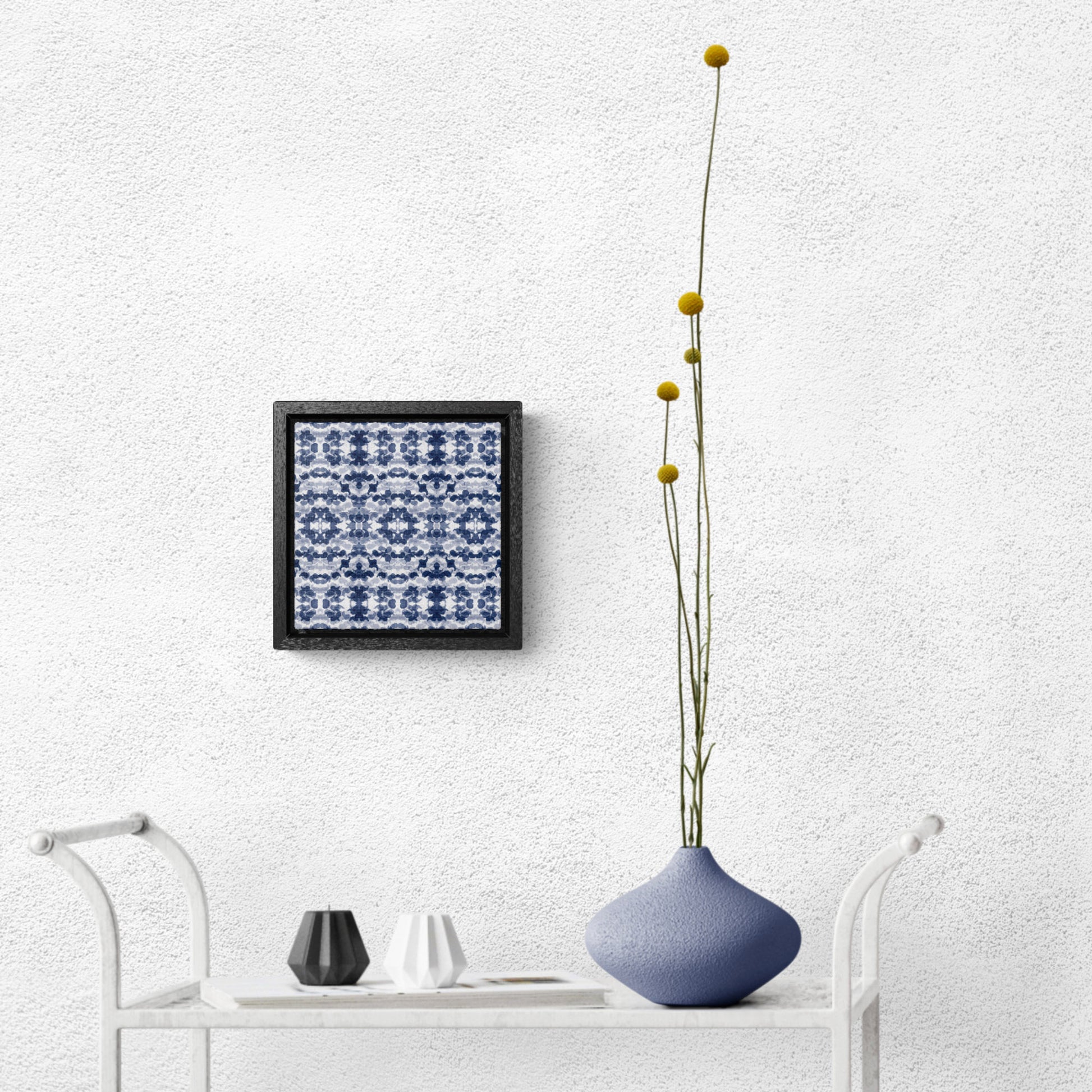 Smalled framed canvas featuring a navy blue paisley pattern hanging over a white tea cart and blue vase