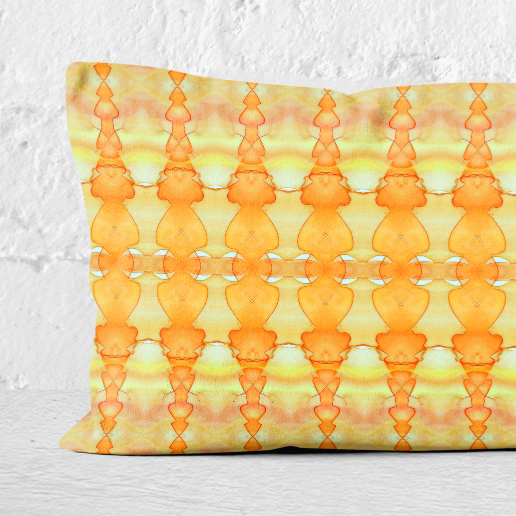 Detail of a rectangular lumbar pillow featuring abstract hand-painted yellow and orange pattern leaning against a white brick wall.