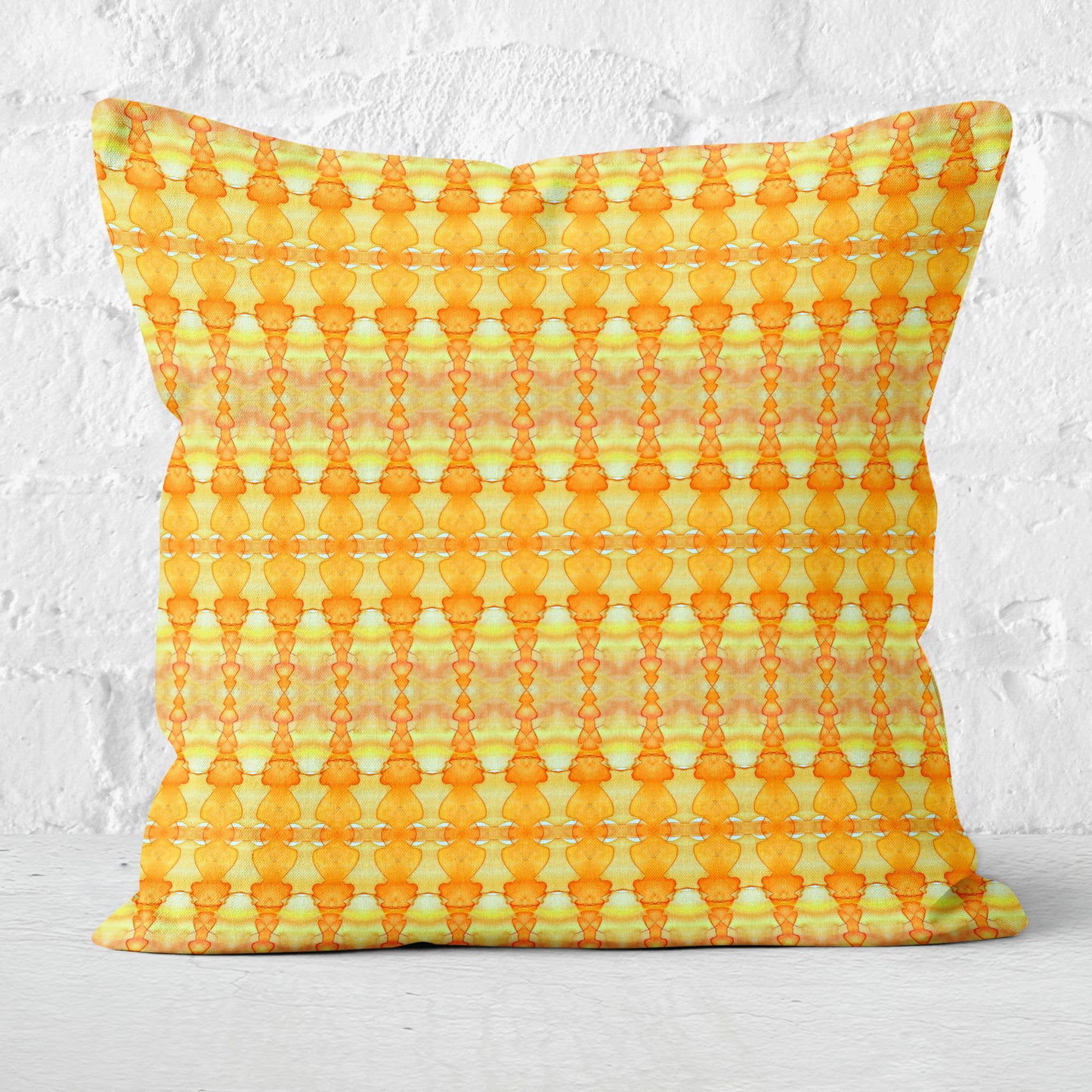 Square throw pillow featuring hand-painted pattern in yellow and orange with a white brick wall in the background