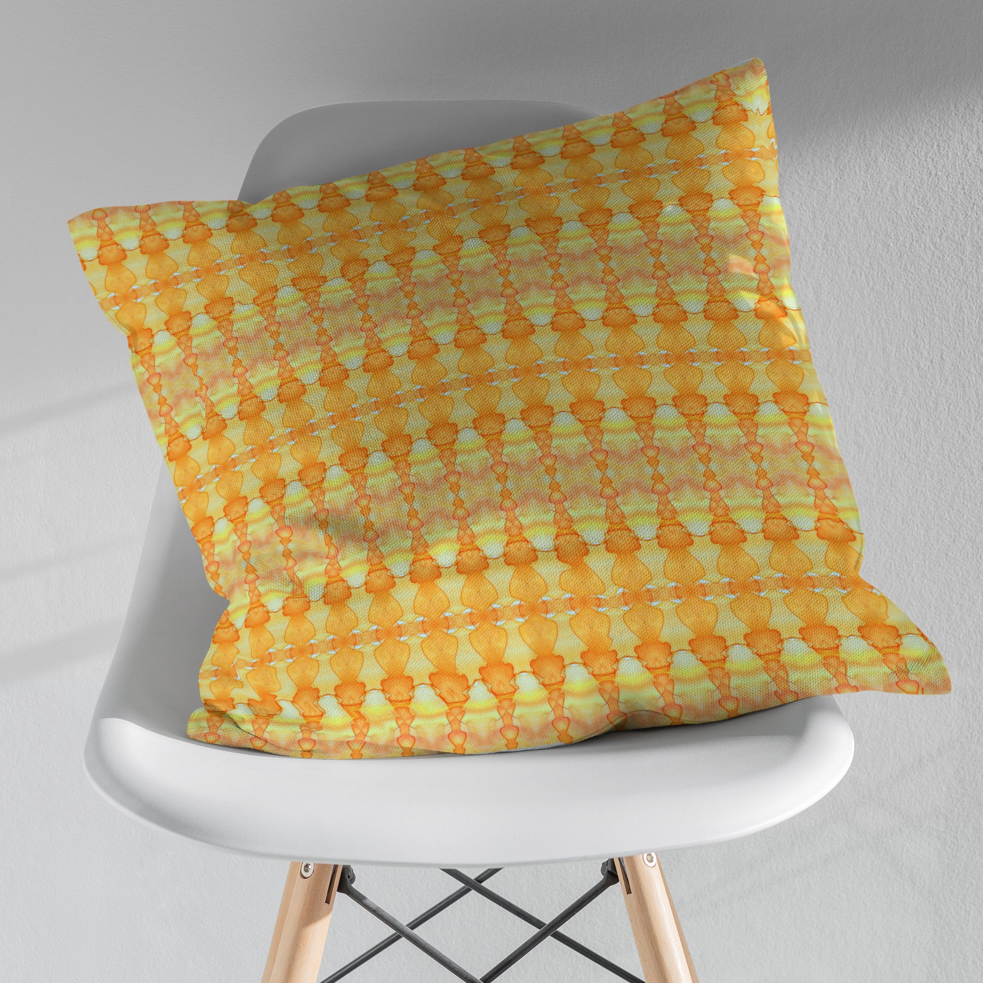 Throw pillow featuring a yellow and orange abstract pattern sitting on a white modern chair