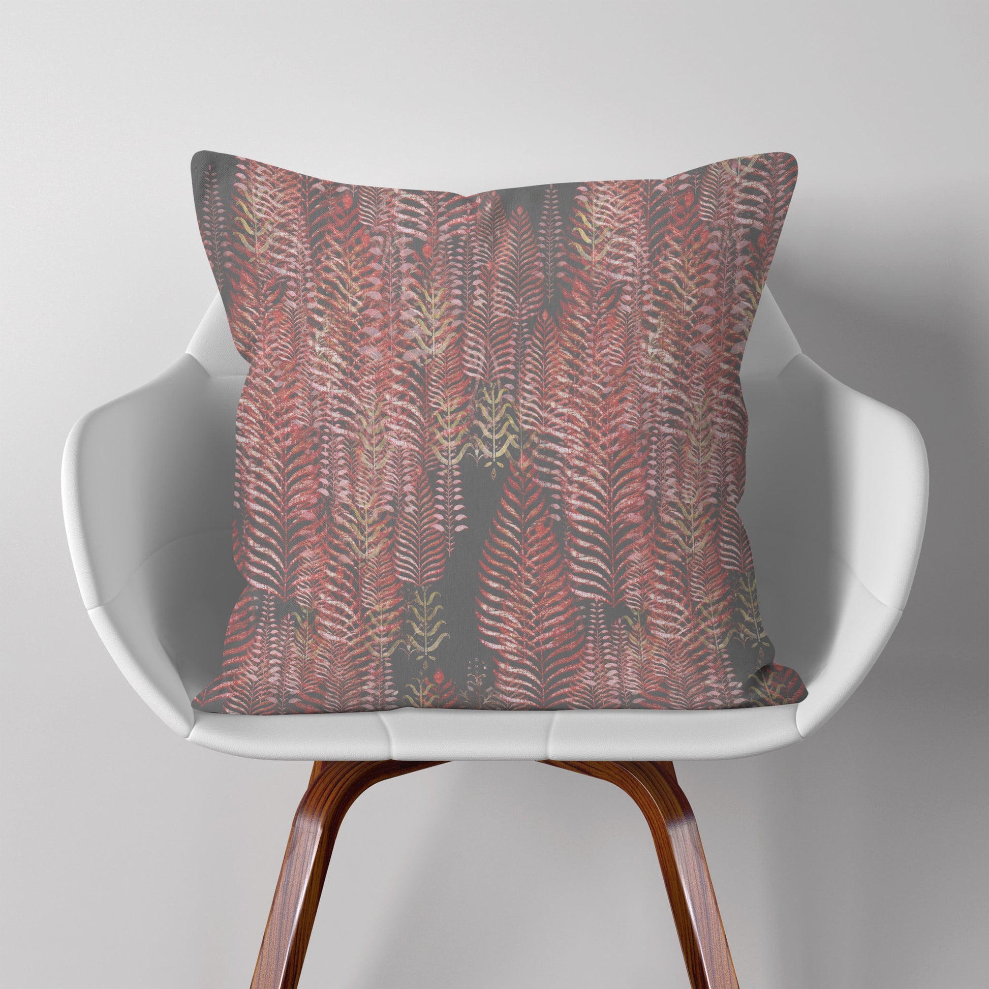 Square throw pillow featuring a block print tree pattern in pink and gray tones, sitting on a modern white chair.