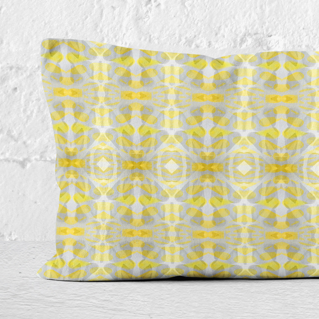 Detail of a rectangular lumbar pillow featuring handprinted striped yellow and grey pattern leaning against a white brick wall.