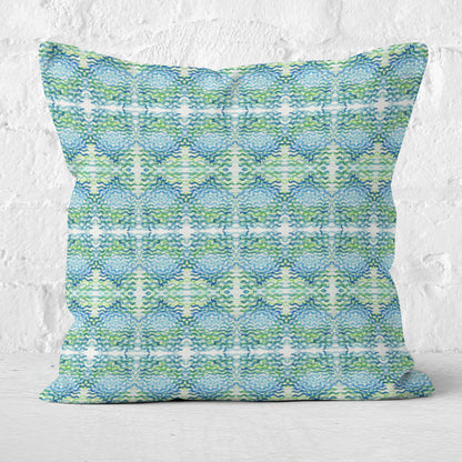Throw pillow featuring a blue and green abstract, hand-painted watercolor pattern, leaning against a white brick wall.