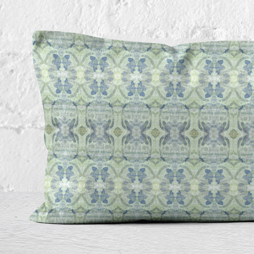 Detail of a lumbar pillow featuring an abstract blue and green floral pattern leaning against a white brick wall