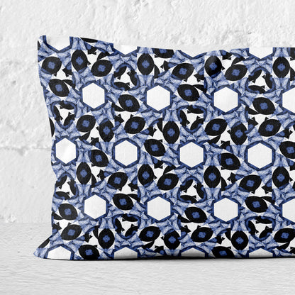 Detail of rectangular lumbar pillow featuring abstract geometric pattern in blue and white leaning against a white brick wall.