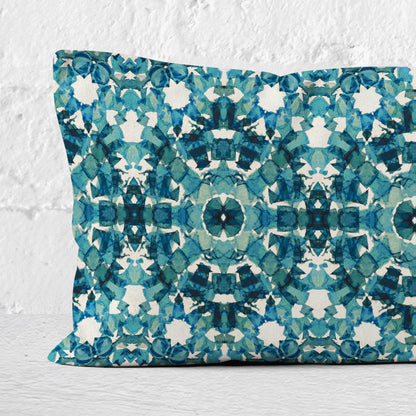 Detail of a rectangular lumbar pillow featuring handprinted pattern in teal leaning against a white brick wall.