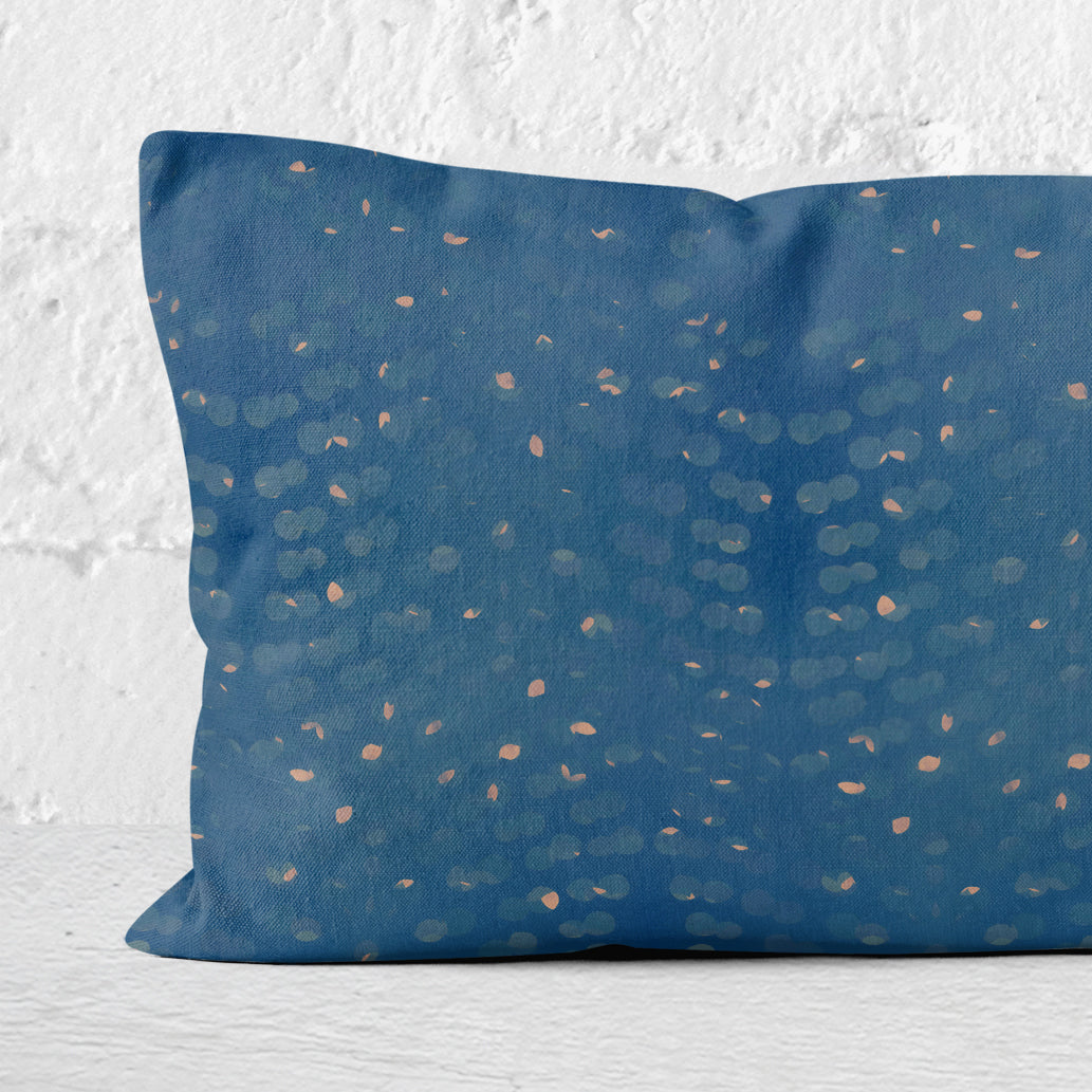 Detail of a rectangular lumbar pillow with hand-painted blue and beige pattern against a white brick wall.