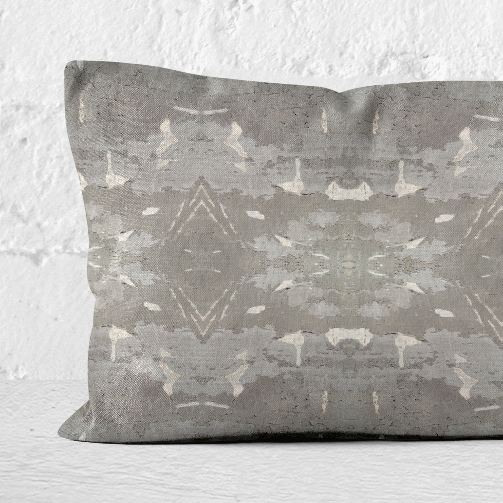 Lumbar pillow featuring a grey abstract geometric pattern leaning against a white brick wall