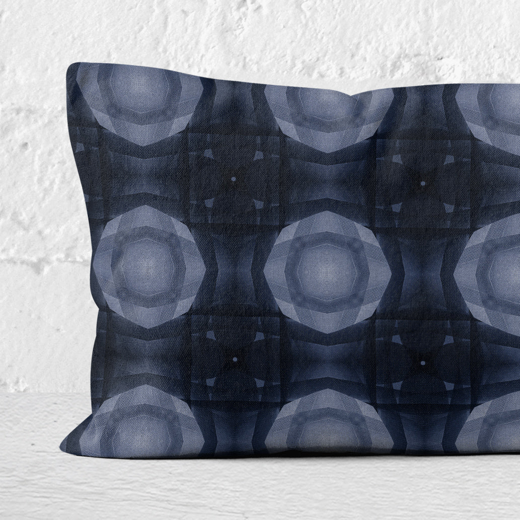 Detail of a 12  inch by 24 inch lumbar pillow featuring a collage-based geometric pattern in shades of blue against a white brick background.