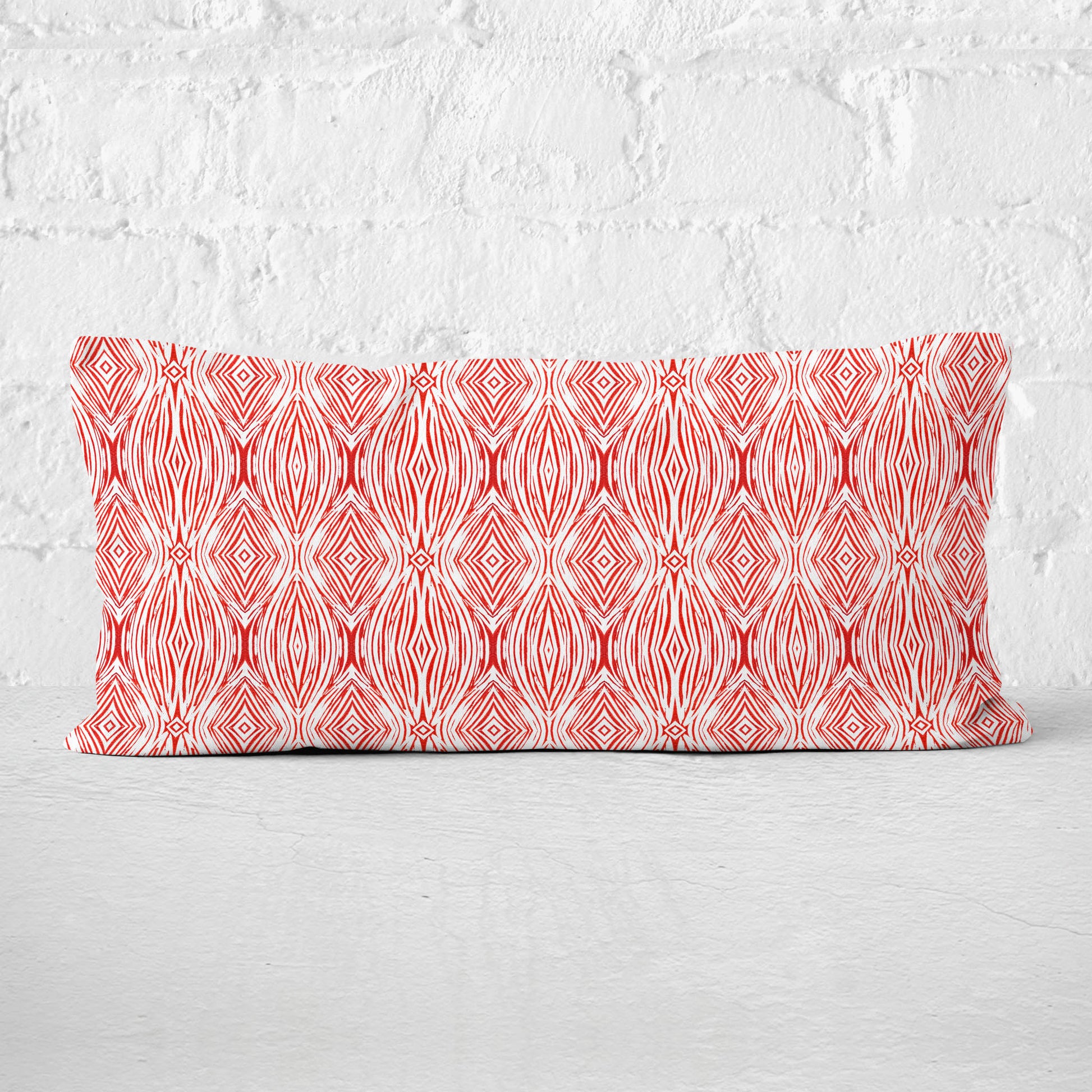 12 x 24 lumbar pillow featuring a red and white abstract linocut pattern leaning against a white brick wall.