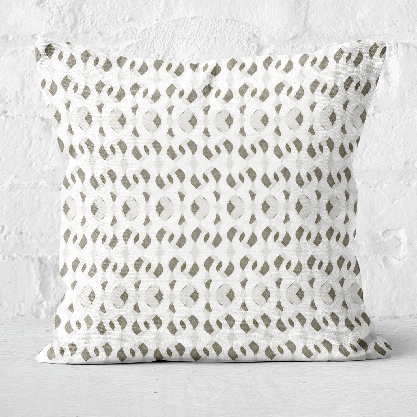 Square throw pillow featuring a painterly abstract pattern in off-white, tan, and gray. Set against a white brick wall.